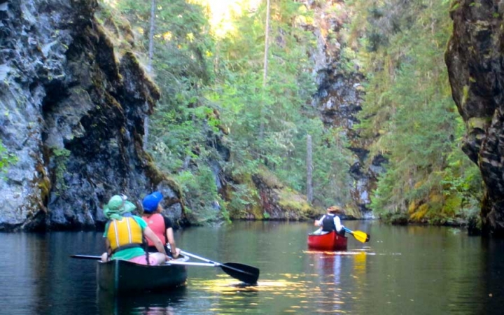 outward bound students paddle two canoes on still water surrounded by greenery